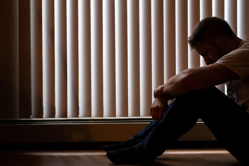 Persoon die vermoeid en nadenkend uit het raam kijkt terwijl zij reflecteert op langdurige stress en emotionele belasting.